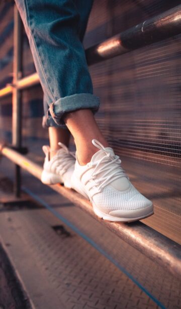 person in blue jeans and white sneakers standing on metal railings