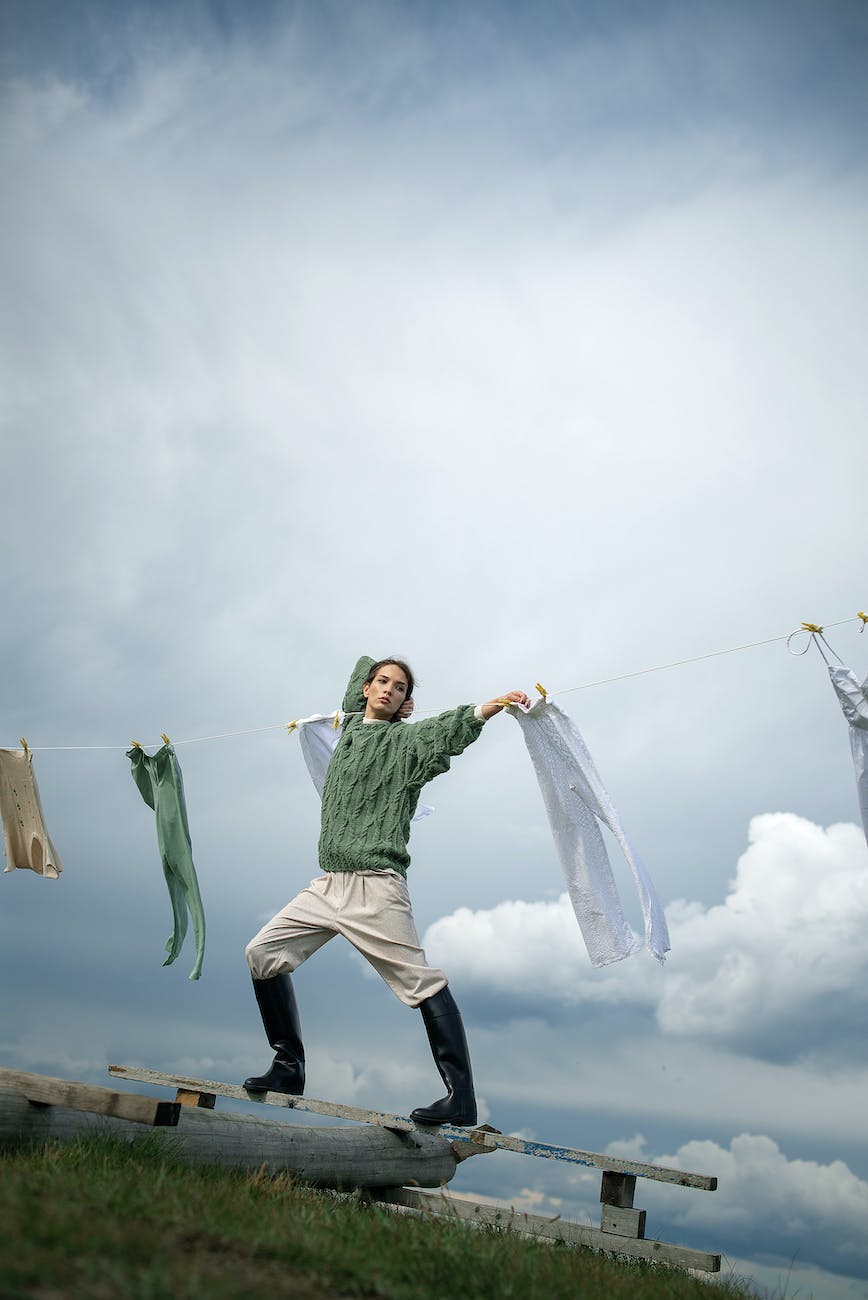 tilt image of a woman wearing green sweater standing on a bench and holding a laundry string