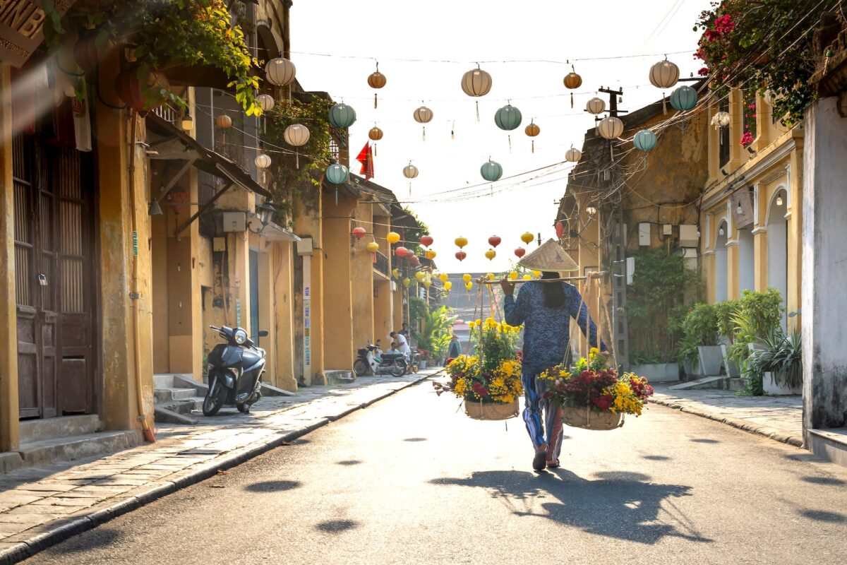 unrecognizable ethnic woman with baskets of flowers strolling on street in vietnam