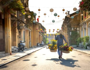 unrecognizable ethnic woman with baskets of flowers strolling on street in vietnam