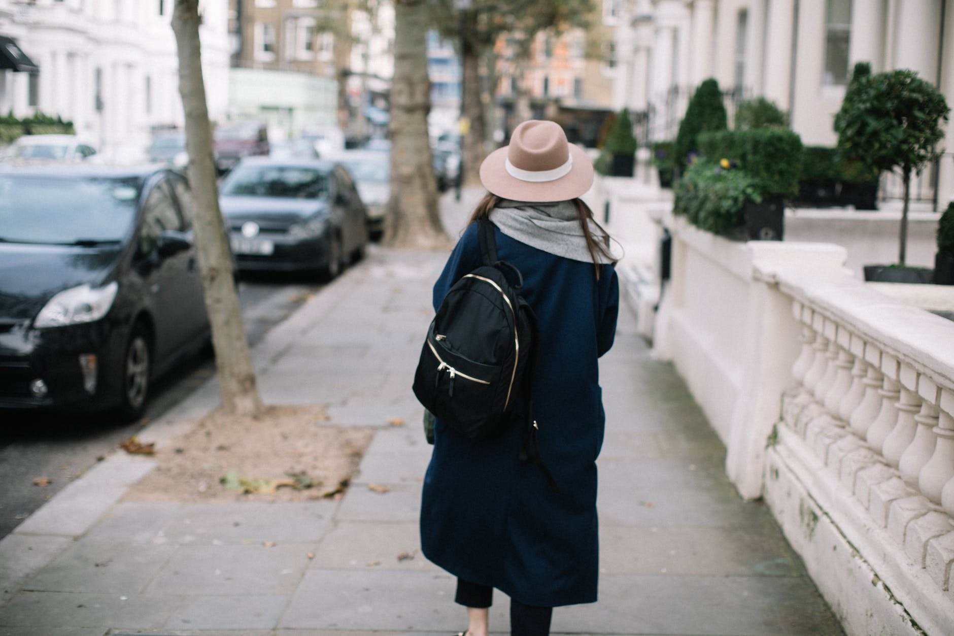 anonyme Frau, die auf dem Bürgersteig im Stadtviertel spazieren geht mit Rucksack auf dem Rücken und großem Hut