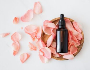 composition of cosmetic bottle with pink rose petals and wooden plate