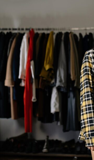 a woman wearing plaid long sleeves shirt and black skirt standing near clothes rack while looking at the camera