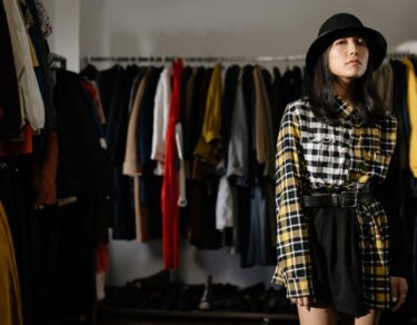 a woman wearing plaid long sleeves shirt and black skirt standing near clothes rack while looking at the camera